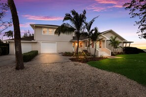 A two-story house with a white exterior, a front garage, and a well-maintained lawn. - Ship Watch: Private Beach, North End, Dog Friendly by Anna Maria Life Vacation Rentals (Anna Maria)