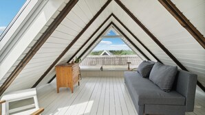 An attic bedroom with a sloped ceiling, a gray sofa, a wooden dresser, and a view of a house through a window. - Stunning home in Glesborg with WiFi (Glesborg)