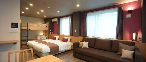 A hotel room with a bunk bed, a sofa, a wooden table, and a large window with curtains.