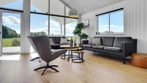 Un salon moderne avec une grande fenêtre, un fauteuil gris, un canap é en cuir noir et une table basse en bois.