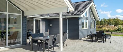 A modern house with a patio area featuring outdoor furniture and a glass door leading to a covered porch.