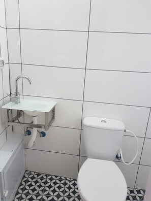 A small, clean bathroom with a white sink, a toilet, and a patterned floor.