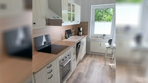 A modern kitchen with white cabinetry, a black induction cooktop, and a window with a view of greenery.
