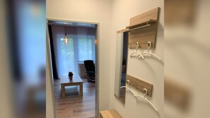 A hallway with a wooden bench, a small table with a flower, and a mirror with hooks on the wall.