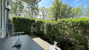 A patio area with a table and chairs, surrounded by lush greenery and a hedge.