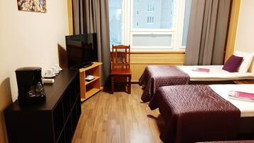 A hotel room with a TV, a coffee maker, a wooden chair, two beds with red bedding, and a window with blinds.