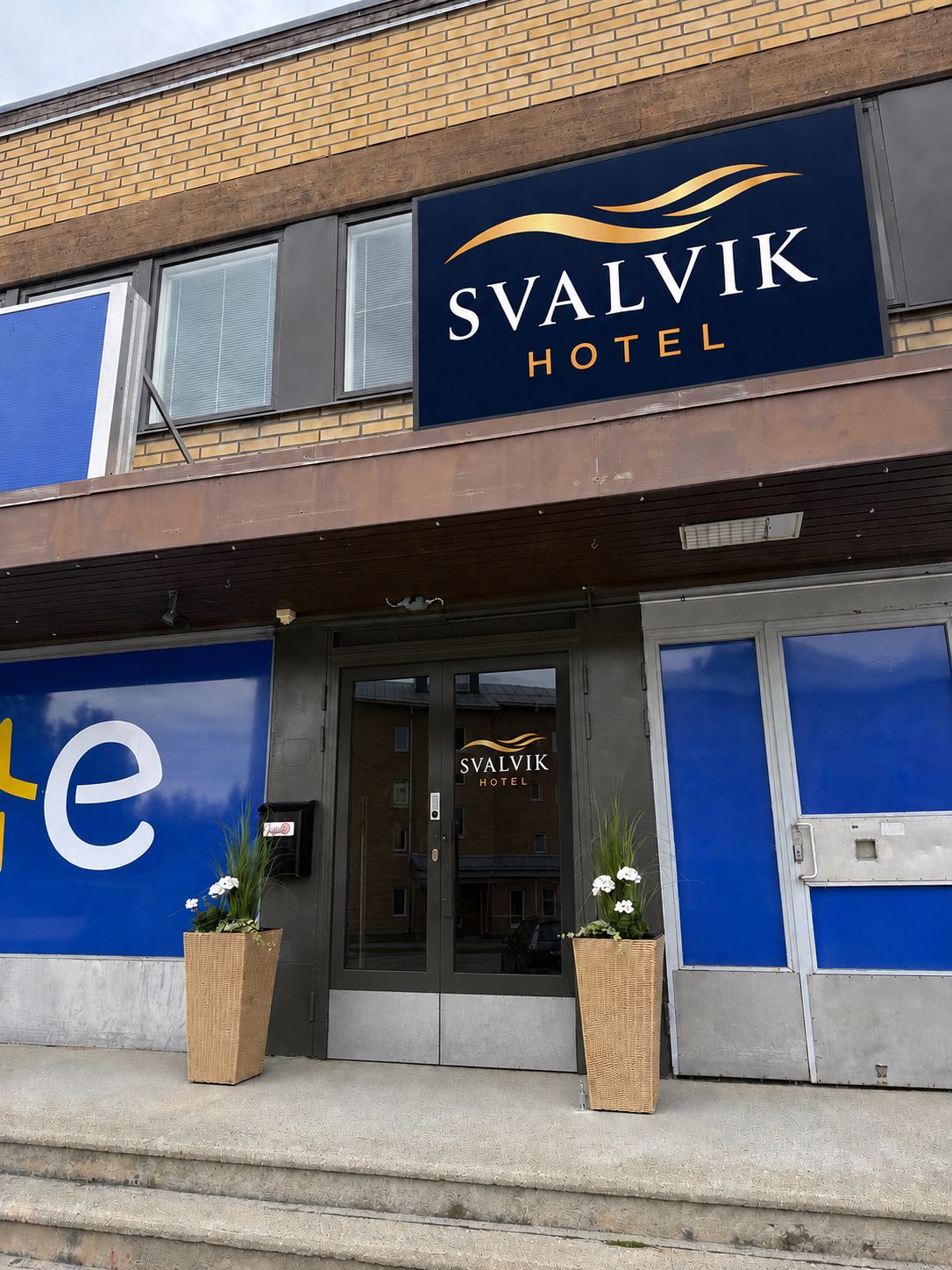 Svalvik-hotellin ulkoasu: selkeä kyltti, lasinen sisäänkäynti ja kaksi ruukussa olevaa kasvia sisäänkäynnin edessä.