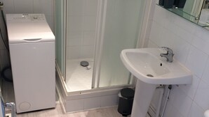 Pieni kylpyhuone, jossa on pyykinpesukone, suihkukaappi, pesuallas ja wc.
