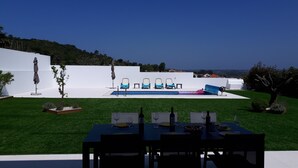Un área junto a la piscina con una mesa de comedor para cuatro personas, una piscina con tobogán y sillas de descanso.
