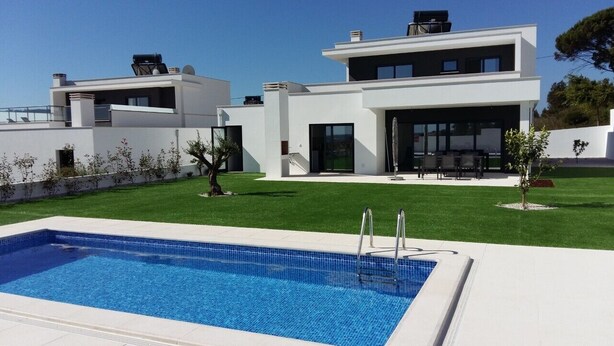 Una casa moderna de dos pisos con piscina, un patio cubierto y un césped bien cuidado.