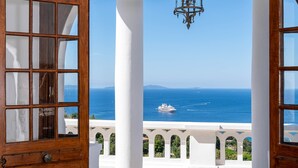Puerta de madera abierta que da a un balcón con suelo a cuadros, con vistas al mar y un barco.