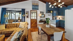 Una sala de estar acogedora con una mesa de comedor de madera, un sofá y una cocina con armarios azules y un refrigerador blanco.