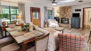 Una sala de estar acogedora con chimenea de piedra, un comedor con mesa y sillas de madera, y un televisor sobre un mueble.