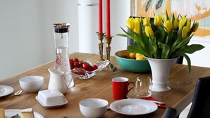 Une table à manger dressée avec différents plats, un pichet, un vase rempli de tulipes jaunes et des bougies rouges.