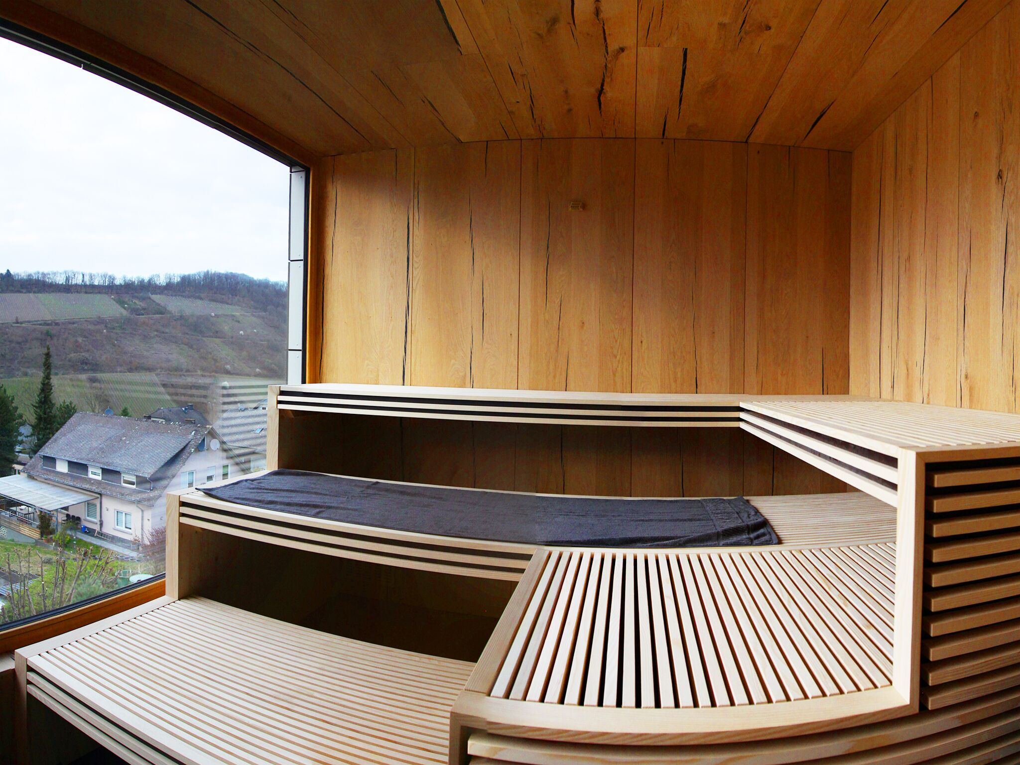 A wooden cabin with a sloped roof, a window overlooking a rural landscape, and a built-in bench with a dark cushion.