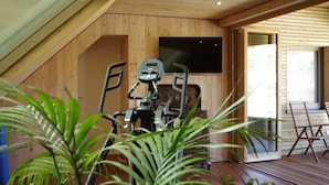 Une pièce dotée d’un ventilateur de plafond, d’appareils de musculation, d’un téléviseur et d’une porte-fenêtre coulissante donnant sur un espace extérieur.