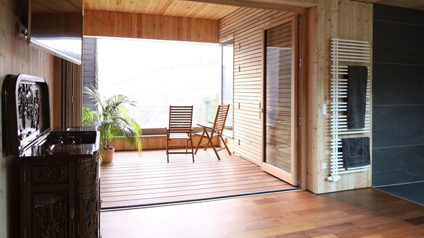 Un intérieur moderne avec un plancher en bois, un plafond en bois, une porte-fenêtre coulissante donnant sur un balcon et une cheminée intégrée.