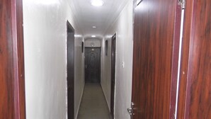 Um corredor estreito com portas de madeira em ambos os lados e chão de azulejos.