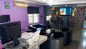Uma área de estar moderna, com televisão de tela plana, assentos confortáveis e um bar com banquetas.