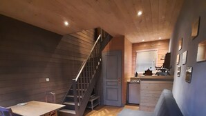 Een knus interieur met een houten vloer, een bank, een eettafel met stoelen, en een keukenhoek met spoelbak en fornuis.