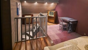 Een kamer met houten plafond, een trap, een bureau met stoel en een bed.