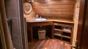 Een houten badkamer met een wastafel, een klein prullenbakje en een plank met flessen.