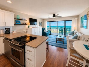 A modern kitchen with a large island, a dining area with a view of the ocean, and a living area with a ceiling fan.