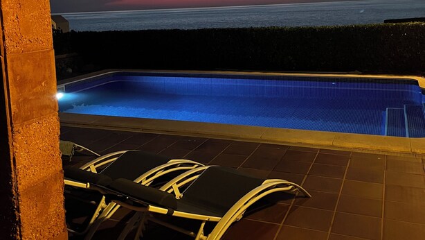 Ein Pool im Freien mit Sonnenuntergangsblick, einer überdachten Sitzgelegenheit und einer gefliesten Terrasse.