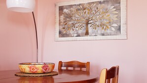 Ein Esstisch mit einer Blumenarrangementschale, zwei Holzsesseln und einem an der Wand hängenden Baumgemälde.