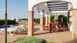 Ein überdachter Außenbereich mit Pool, Liegestühlen und einem Tisch mit Stühlen.