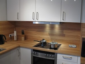 A modern kitchen with white cabinets, a stainless steel stove, and a wooden countertop. - Spacious vacation apartment with balcony (lake view), garden and direct lake access (Ascheberg)