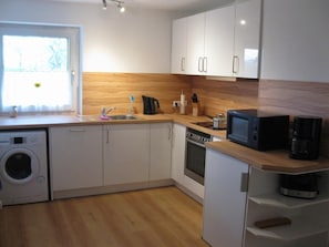 A compact kitchen with white cabinets, a built-in oven, a microwave, and a washing machine. - Spacious vacation apartment with balcony (lake view), garden and direct lake access (Ascheberg)