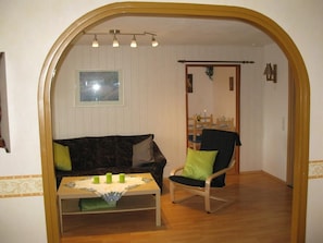 A cozy living room with a wooden floor, a dark patterned sofa, a green armchair, and a small table with a tablecloth. - Spacious vacation apartment with balcony (lake view), garden and direct lake access (Ascheberg)