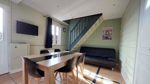 A dining area with a wooden table and chairs, a sofa, a staircase, and a wall-mounted TV.