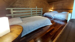 A cozy attic bedroom with wooden walls and floors, featuring two beds with white bedding and a wooden headboard.