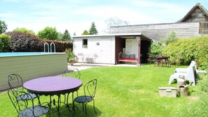 A backyard with a round table and chairs, a small shed, and a wooden building.