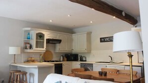 A compact kitchen with white cabinets, a central island, and a dining area with a table and chairs. - Courtyard cottage in Slapton, South Devon. 10 minutes drive to beach (Kingsbridge, Devon)