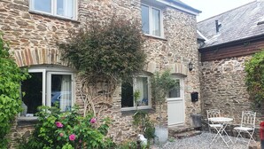 A stone building with a small patio area, including a white metal table and chairs, and a variety of plants and flowers. - Courtyard cottage in Slapton, South Devon. 10 minutes drive to beach (Kingsbridge, Devon)