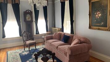 A living room with a pink sofa, a wooden chair, a chandelier, a clock, and a painting on the wall.