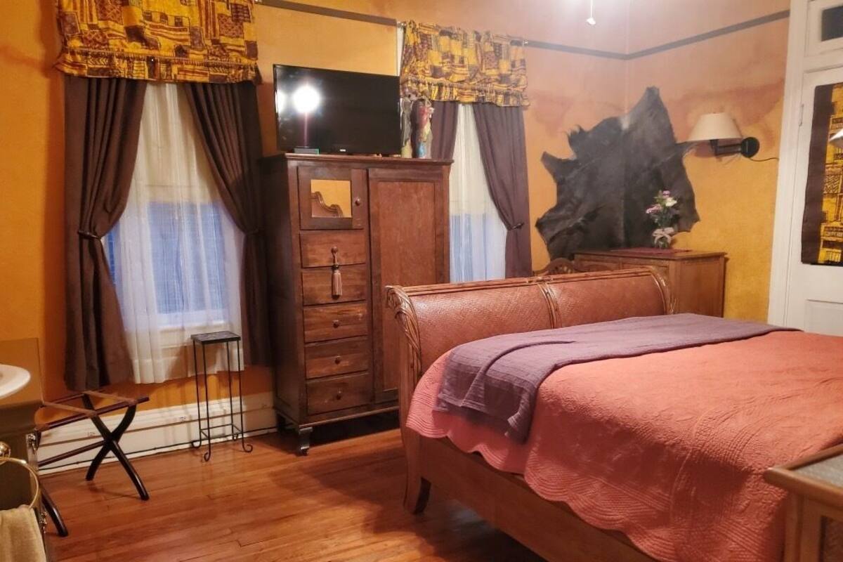 A bedroom with a wooden bed, a dresser, a television, and a large wall painting.