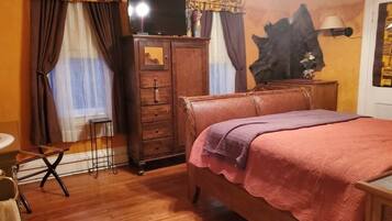 Un dormitorio con una cama de madera, un aparador, un televisor y un cuadro grande en la pared.