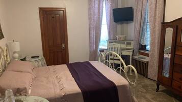 Un dormitorio con cama, cómoda, espejo, televisión y ventana con cortinas.