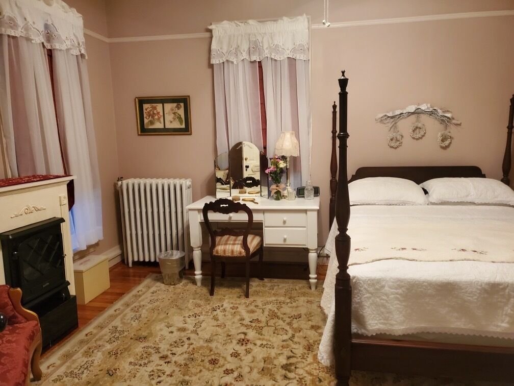 A bedroom with a bed, a desk, a chair, a radiator, and a fireplace.