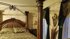 Een slaapkamer met een groot bed, een houten hoofdbord, een nachtkastje met een lamp en een decoratief object aan de muur.