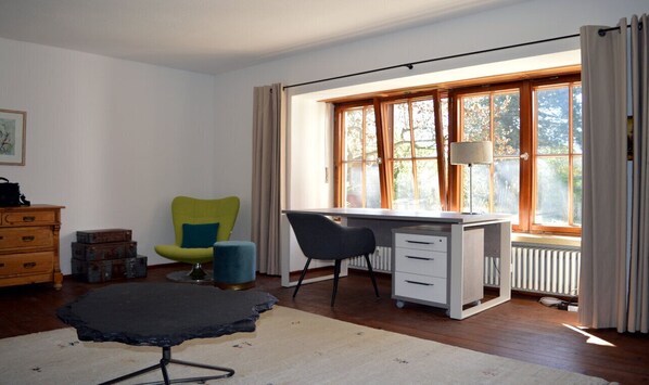 Ett rum med ett skrivbord, en stol, en lampa, ett element och ett fönster med gardiner.