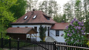 Une maison blanche avec un toit recouvert de tuiles rouges, une clôture en bois et un petit porche.