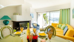 A bright living room with a yellow sofa, a fireplace, and a dining table set with glasses and bottles. - Lovely apartment for 4 guests with WIFI, A/C, TV, terrace and pets allowed (Le Grau-du-roi)