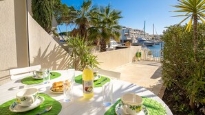 A table set for two with a view of a marina and boats in the background. - Lovely apartment for 4 guests with WIFI, A/C, TV, terrace and pets allowed (Le Grau-du-roi)