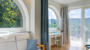 A modern room with a wooden bench, a white sofa, a desk with a chair, and large windows offering a view of greenery. - Beautiful private villa for 6 guests with A/C, WIFI, TV, patio and panoramic view (Casalborgone)