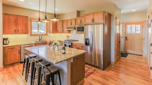 A kitchen with wooden cabinets, a stainless steel refrigerator, granite countertops, and pendant lighting.